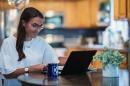 Woman working on computer at a kitchen table with a UNH mug in the foreground